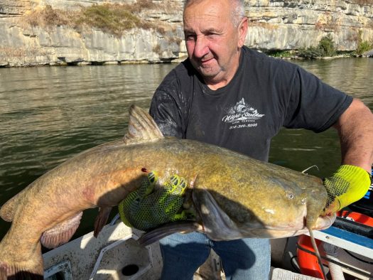 A man on a catfish charter holding a large catfish on a boat.