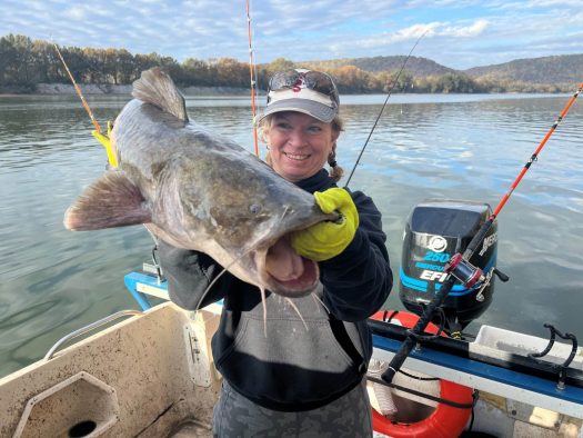 A woman proudly displays a catfish caught on a charter fishing boat.