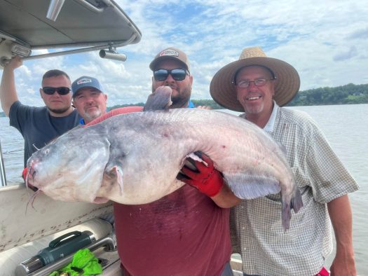 Three men holding up a catfish on a boat during their catfish charter.