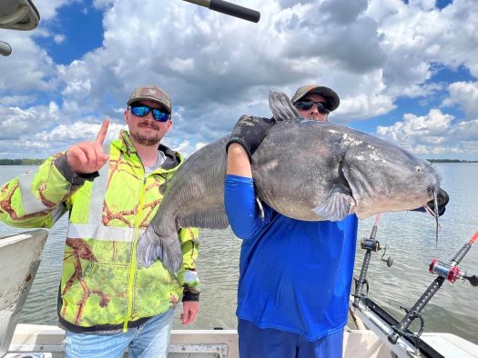 A catfish charter with two men proudly displaying their impressive catch on a boat.