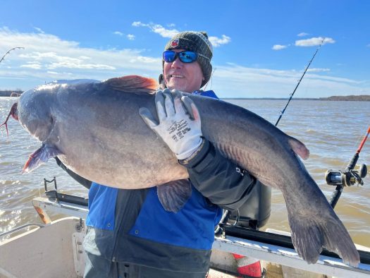 A man proudly displays a sizable catfish caught during a catfish charter excursion on a boat.