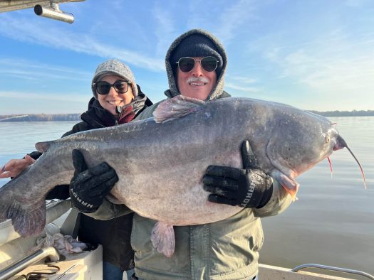 Two people proudly displaying a massive catfish during a thrilling catfish charter expedition.